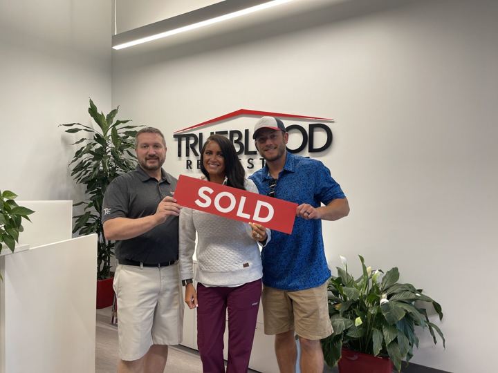 Wes and two people holding a red SOLD sign in the Trueblood Real Estate office