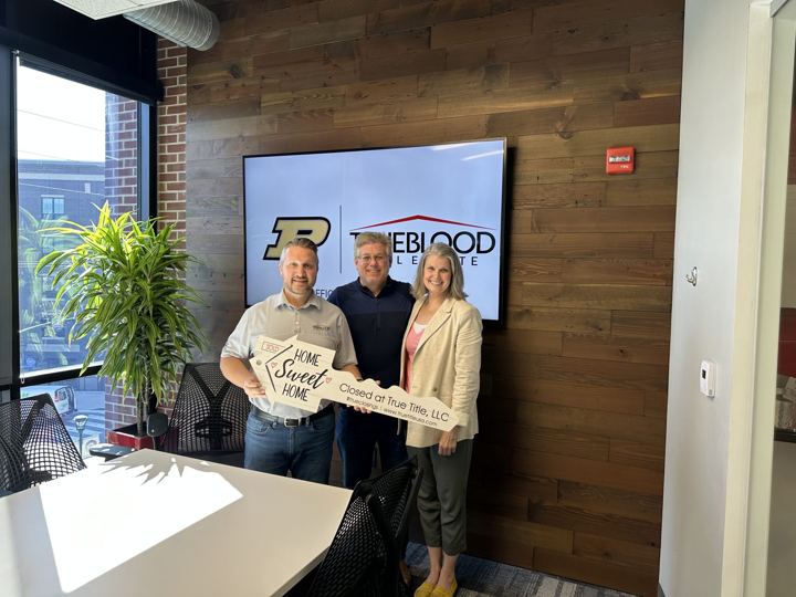 Wes and two people holding a Home Sweet Home key sign in a title company conference room