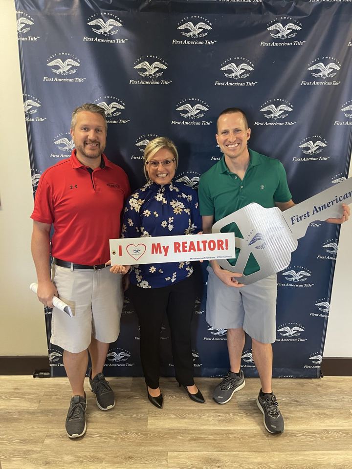 Wes with two people holding an I love my REALTOR sign and a giant key at a title company