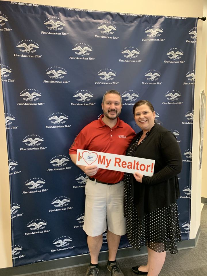 Wes and a woman holding an I love my REALTOR sign in front of a title company backdrop