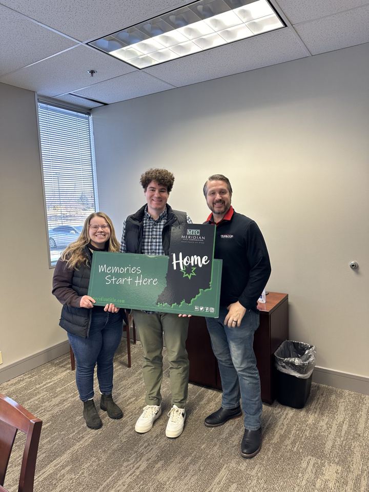 Wes with two people holding a Home sign at a title company